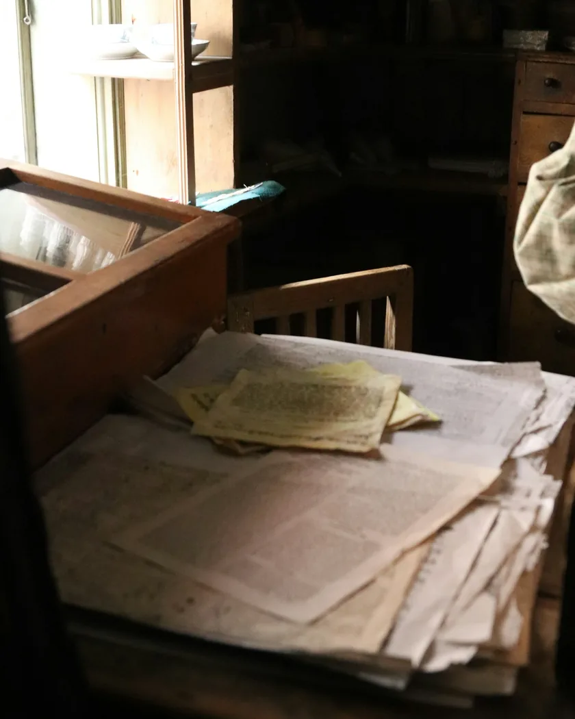 Listy papíru rozložené na dřevěném stole v tlumeném světle dílny